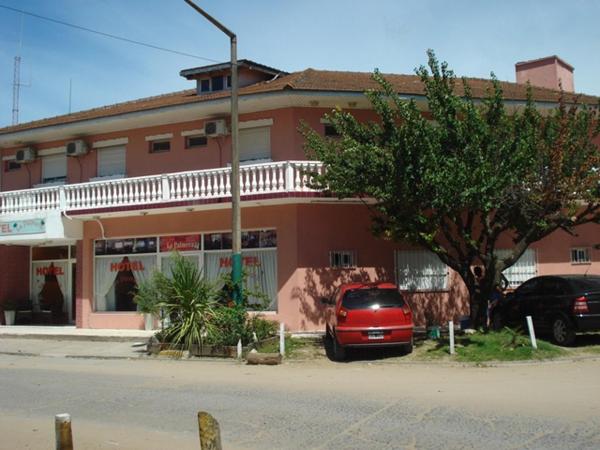 un coche rojo aparcado frente a un edificio del Hotel La Palmera de Villa Gesell